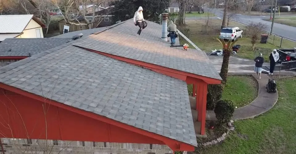 Roofers working across a gray shingle roof