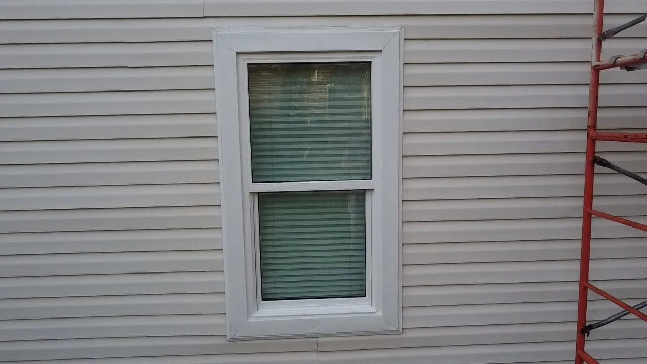 New siding installed around a window, ladder at the side